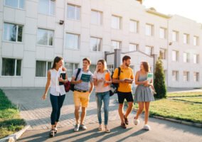 Five friendly students are walking after they passed test outside the college building and discuss the project